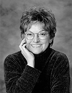 a black and white photo of Sara Rath. She has glasses and is wearing a dark turtleneck sweater. Photo credit: Nancy Rubly 