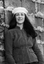 The author, Paola Corso, leans against a brick wall, she is wearing a light colored béret.