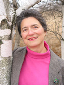 photo of the author, Judith Strasser, outdoors, by a birch tree. She wears a bright turtlenceck and a grey blazer.