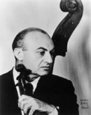 This is a black and white photo of Louis Kaufman, with a violin in hand. Behind him we see the scroll of a string bass.
